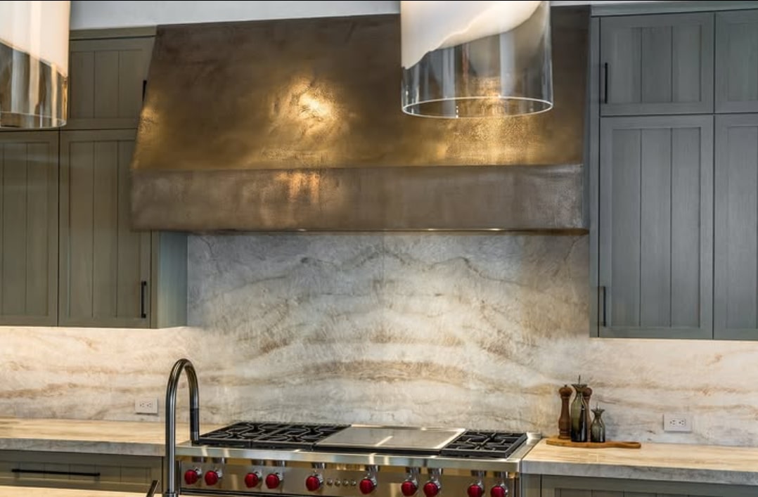 A hand-plastered kitchen hood in a bronze finish above a range, with a marble backsplash